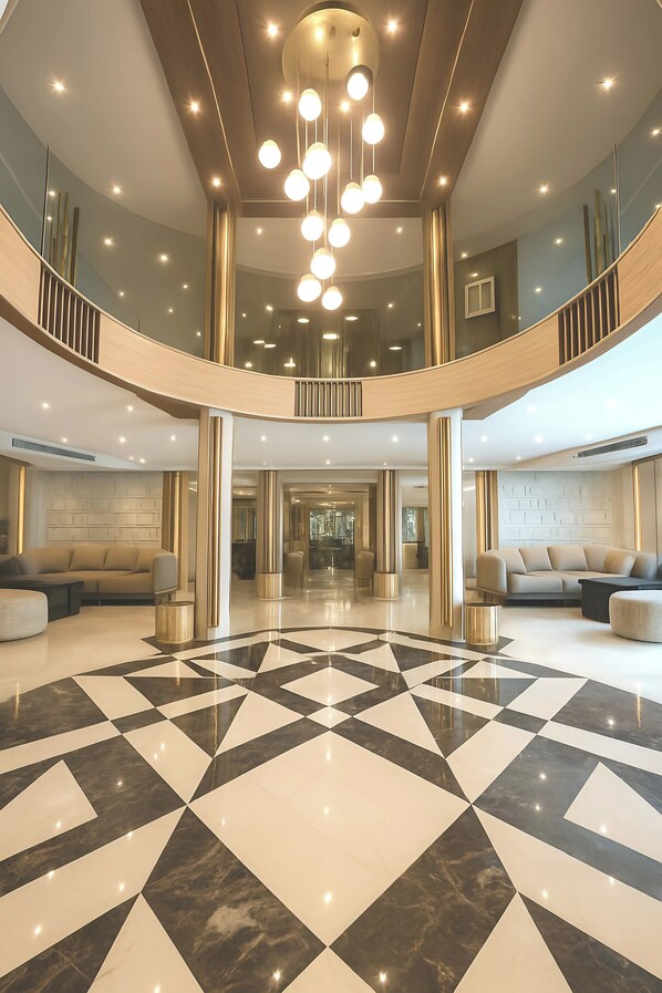 A spacious lobby with a checkered floor, a central staircase, and a modern chandelier.