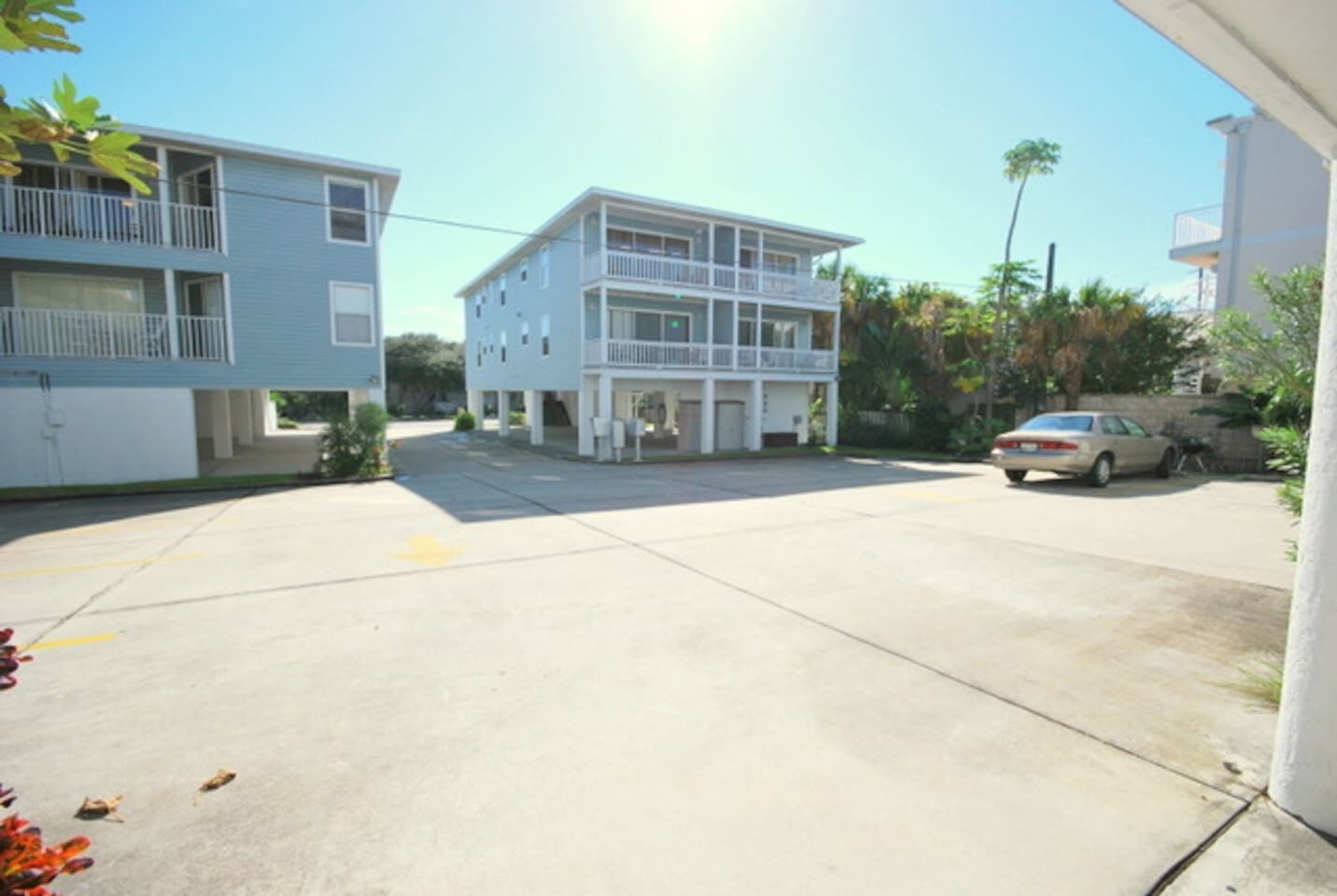 A two-story building with a balcony on the upper floor, a parking lot in front, and a car parked to the right.
