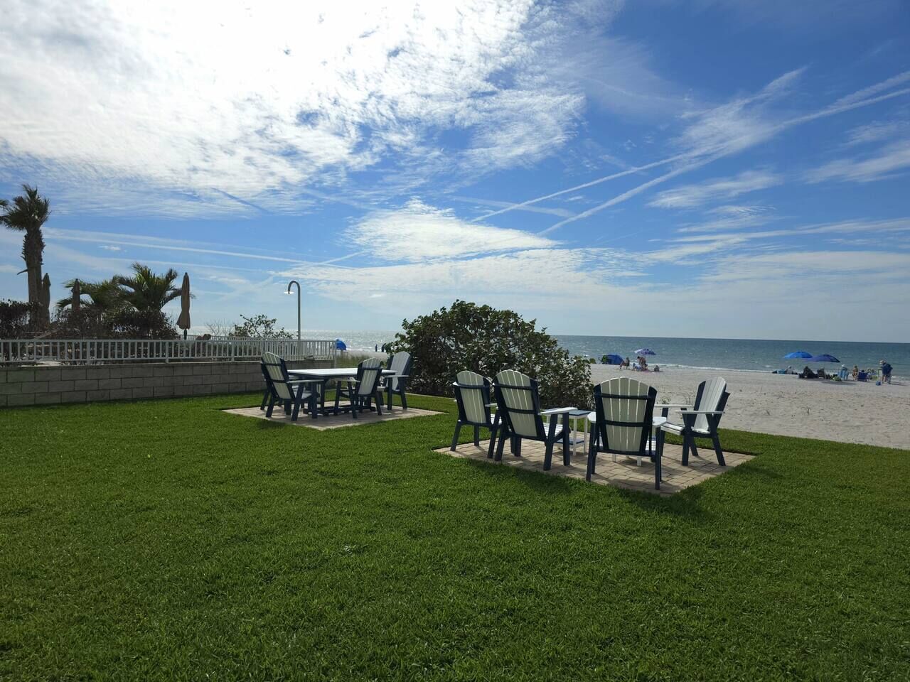 Un espace extérieur aménagé avec des tables et des chaises, une pelouse verdoyante et une vue sur la plage.