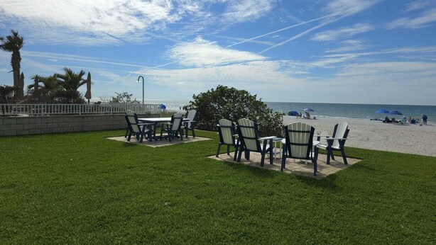 Een terras met tafels en stoelen, een gazon en uitzicht op het strand.