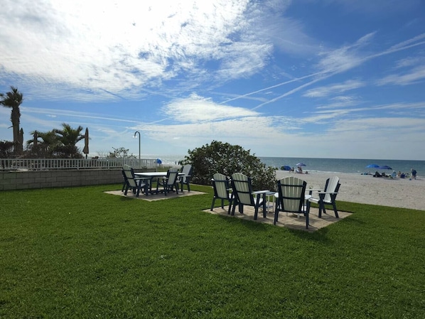 An outdoor seating area with tables and chairs, a grassy lawn, and a view of the beach.