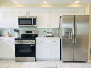 A kitchen with white cabinets, stainless steel appliances including a microwave, oven, and refrigerator, and a tiled backsplash. - Sea Isles Unit P - Beach Front! Private Elevator! (Indian Rocks Beach)