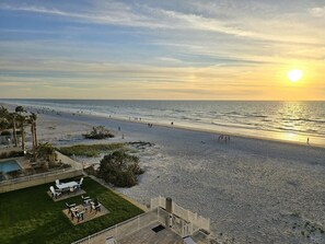 Vista da praia com área de piscina, cadeiras de sol e escadaria para um deck.