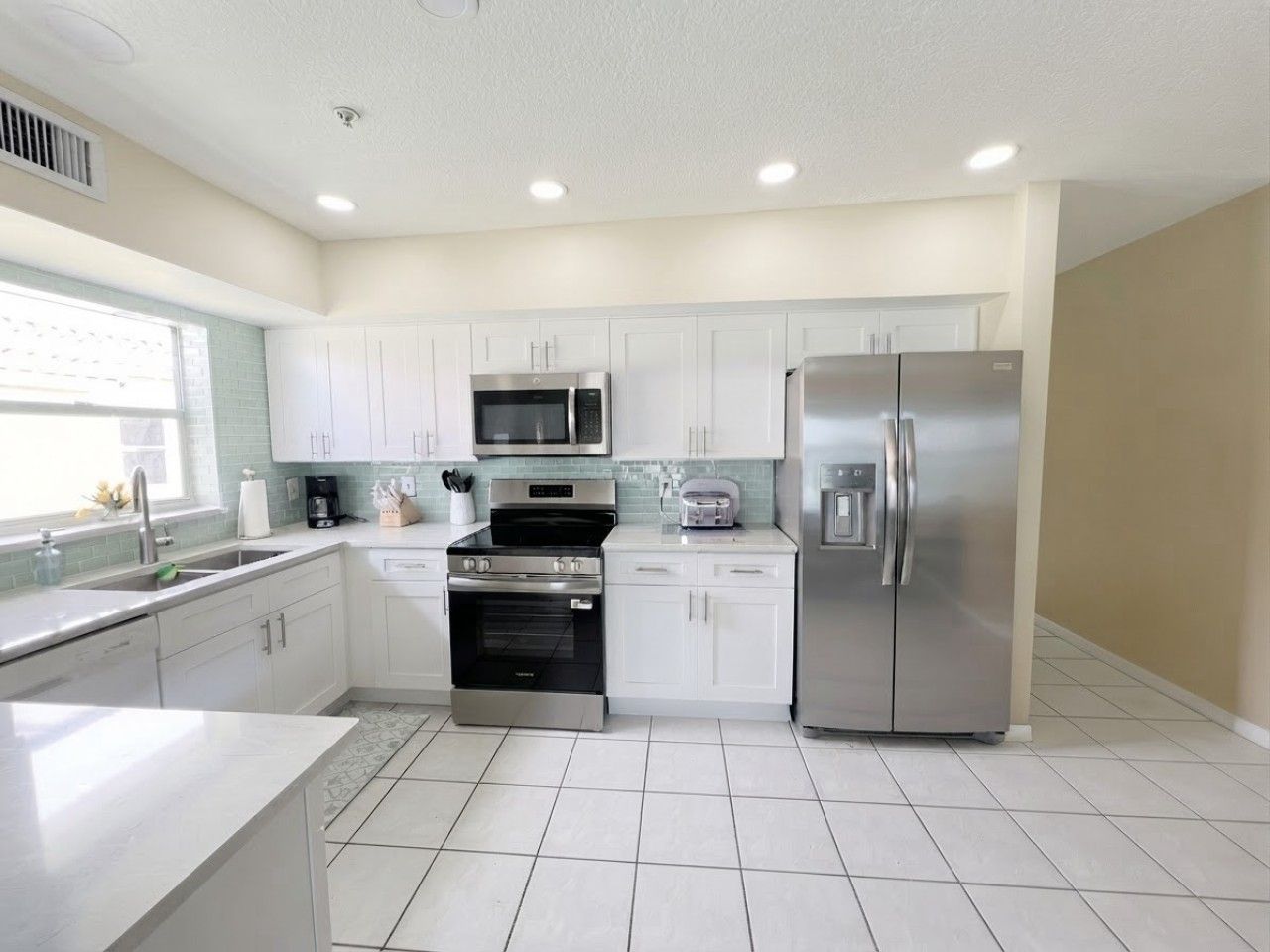A modern kitchen with white cabinets, stainless steel appliances, and a tiled floor.
