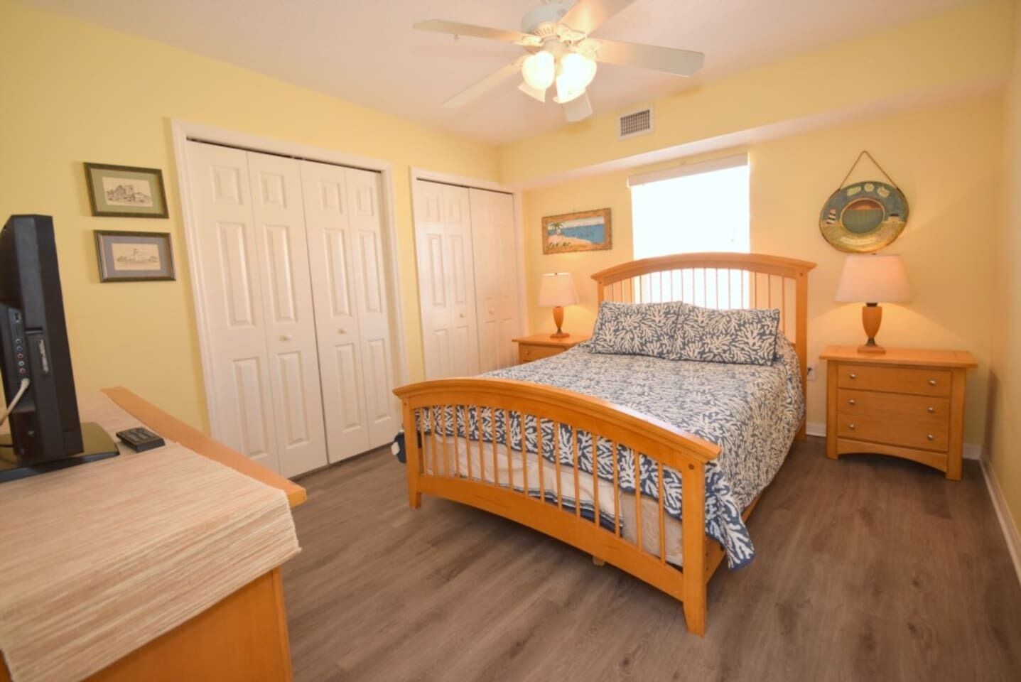 A bedroom with a bed, bedside tables, a ceiling fan, a window, and a door.