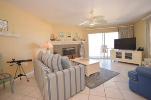 A living room with a sofa, a coffee table, a television, and a fireplace. - Sea Isles Unit P - Beach Front! Private Elevator! (Indian Rocks Beach)
