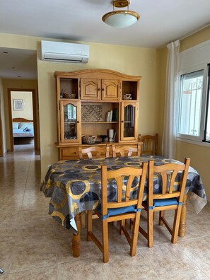 A dining area with a table set for four, wooden chairs, a cabinet with glass doors, and an air conditioning unit on the wall. - Soothing villa 300 metres from the beach (Les Tres Cales)