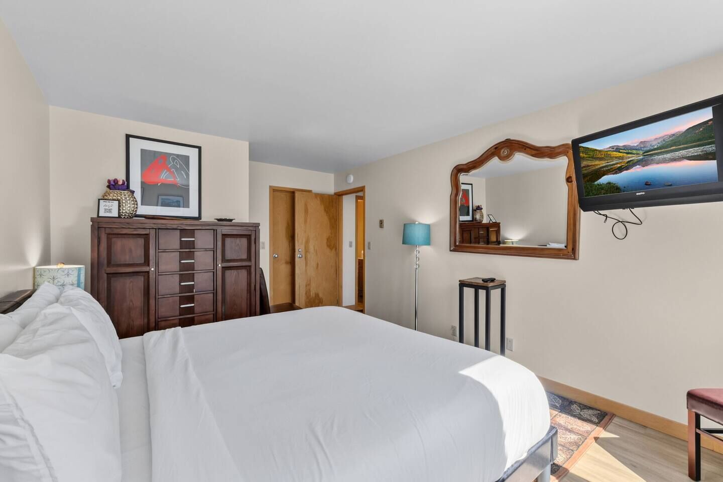 A hotel room with a large bed, a wardrobe, a television, and a mirror.