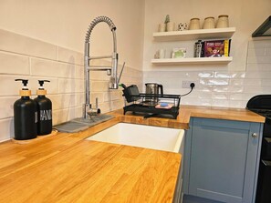 A kitchen with a wooden countertop, a stainless steel sink, a kettle, and a coffee maker. There are two black bottles on the left. - Save 25% OFF Monthly| Sharrow Retreat | Sleeps 4 (North Yorkshire)