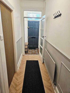 A hallway with a black mat, a door, a radiator, and a wall-mounted coat rack. - Save 25% OFF Monthly| Sharrow Retreat | Sleeps 4 (North Yorkshire)
