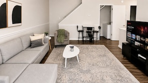 A living room with a sofa, coffee table, and TV. There's a staircase leading to another room.