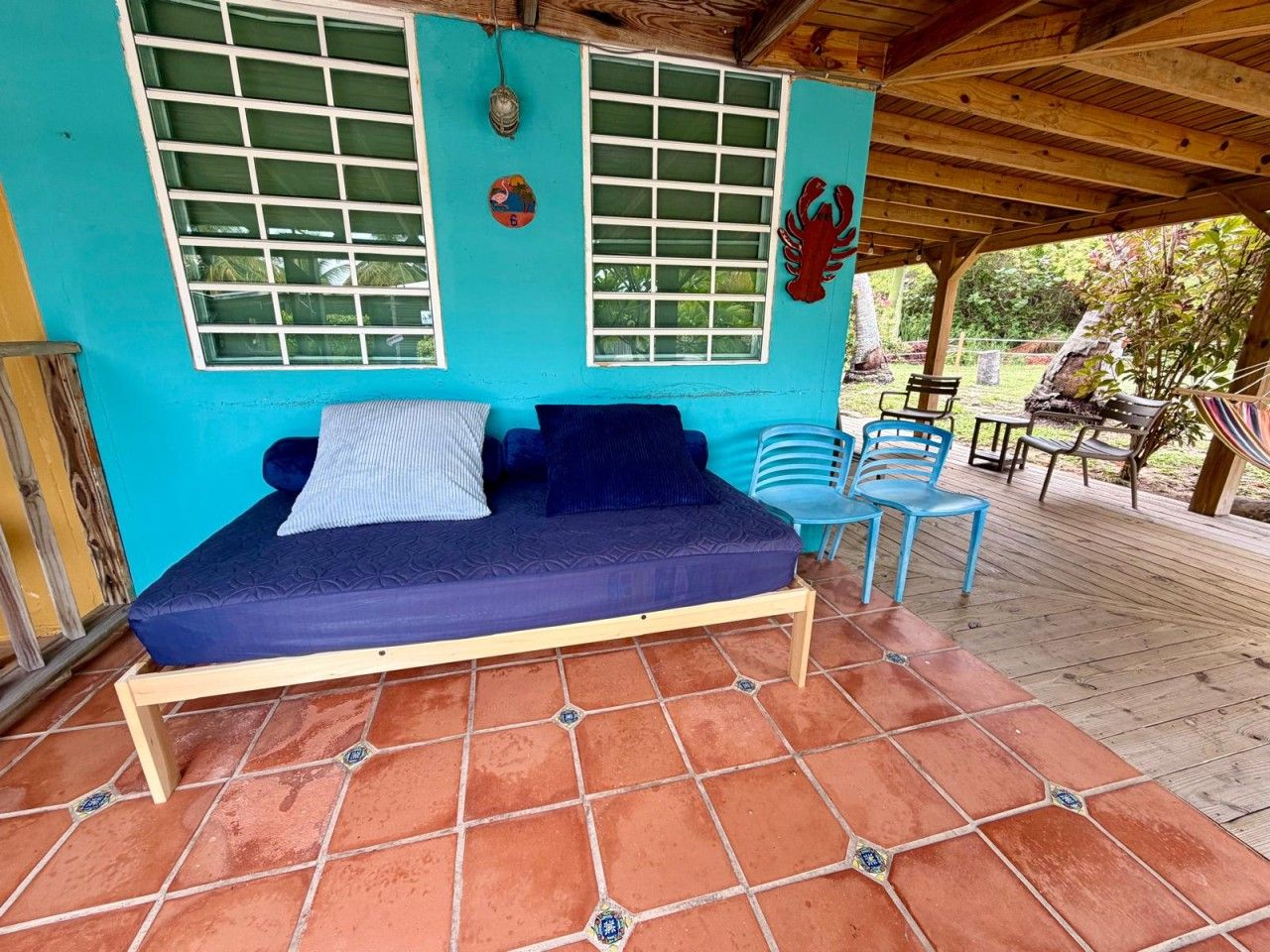 Ein blaues Schlafsofa mit Kissen, eine Holzbank und eine geflieste Terrassenfläche.