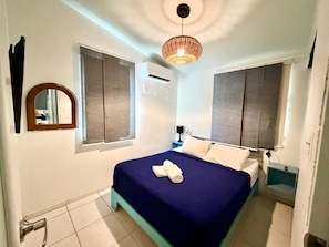 A bedroom with a bed, two windows, a mirror, a bedside table, and a hanging light fixture. - Villa 6 Flamenco Beachfront Villas (Flamenco)