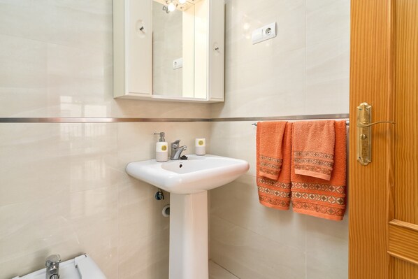 A bathroom with a white sink, a mirror, and an orange towel.