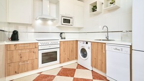 Una cucina moderna con mobili bianchi, un forno a microonde, una lavatrice e una lavastoviglie.