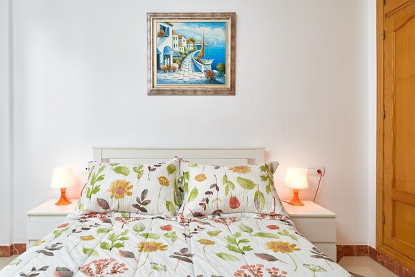 Ein Schlafzimmer mit einem Bett, zwei Nachttischlampen, einem Bild über dem Bett und einem Holzschrank.
