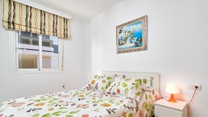Una camera da letto con un letto, un comodino con lampada, una finestra con persiane e un quadro appeso al muro.