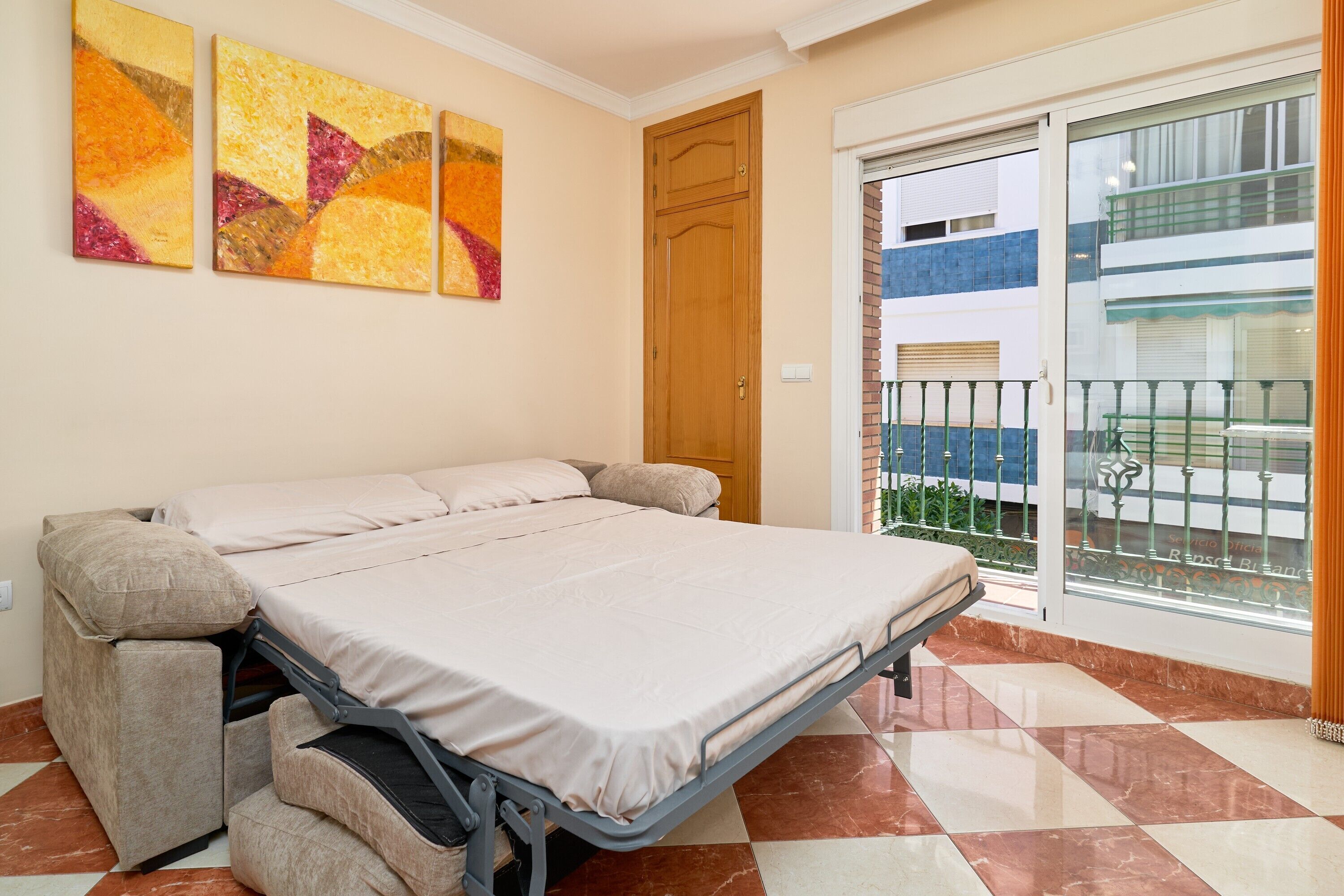 A room with a bed, a sliding glass door to a balcony, and abstract wall art.