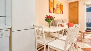 Una cucina moderna con elettrodomestici bianchi, una zona pranzo con sedie bianche, un tavolo e un vaso con fiori.