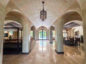 A spacious interior with arched ceilings, a central chandelier, and a view to an outdoor area. - Fantastic 6-bedroom Italian-Inspired Luxury Estate on the Reserva de Golf (CP)
