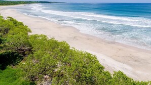 Una playa con agua azul cristalina, orilla de arena y vegetación verde.