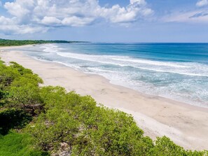 A beach with clear blue water, sandy shore, and green vegetation. - Fantastic 6-bedroom Italian-Inspired Luxury Estate on the Reserva de Golf (CP)