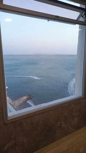 Une vue à travers une fenêtre sur une zone côtière, avec un rivage rocheux et une mer calme.