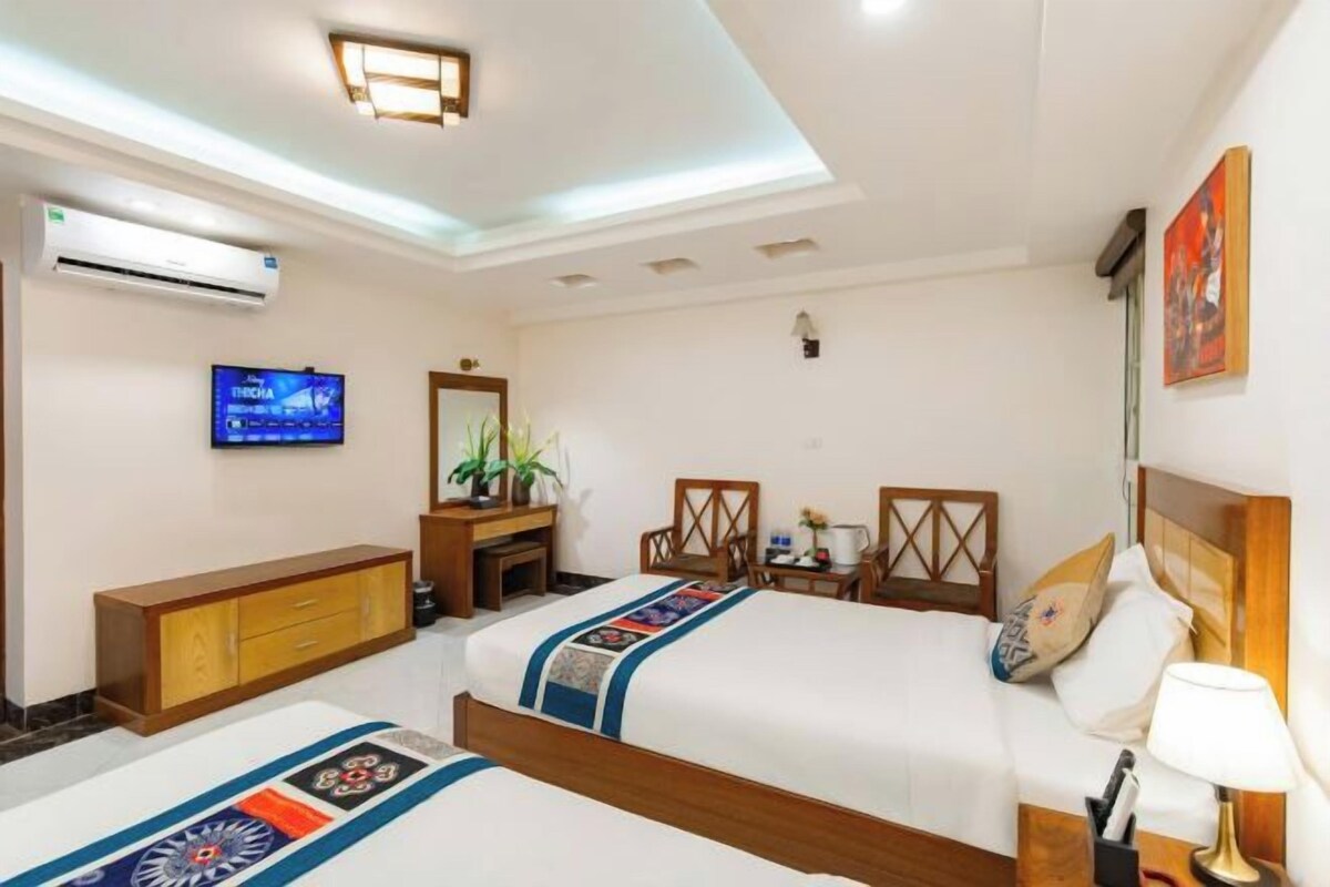 A hotel room with two beds, a TV, a desk with a chair, a mirror, and a wall-mounted air conditioner.