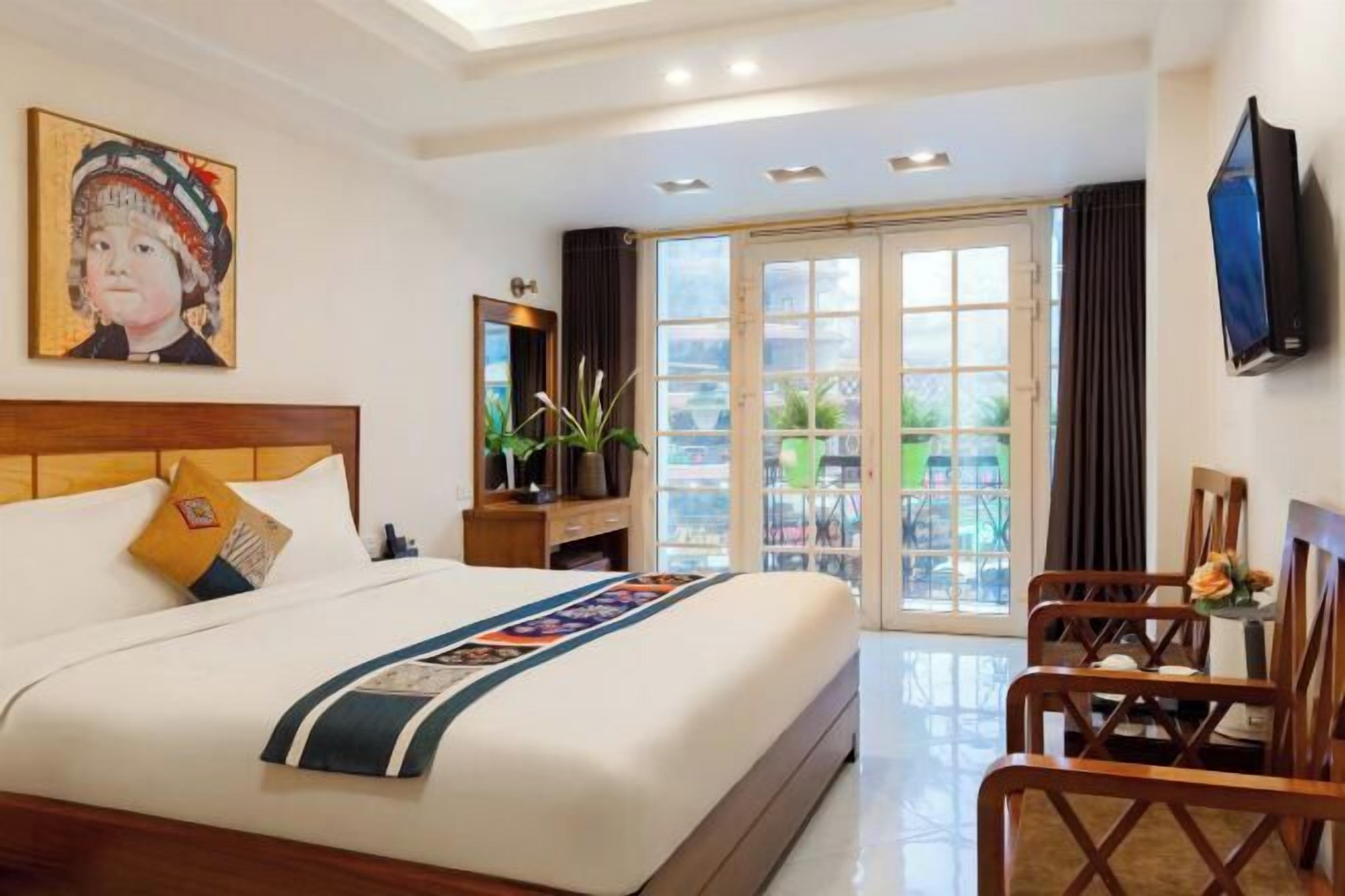 Habitación de hotel con una cama grande, televisor, balcón con vistas y un cuadro en la pared.