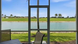 A view from a covered area with a table and chairs, overlooking a golf course and a body of water. - #914 - First Floor Golf and Lake View -Sleeps 6 (Naples)