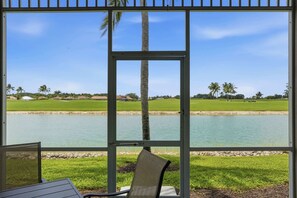 A view from a covered area with a table and chairs, overlooking a golf course and a body of water. - #914 - First Floor Golf and Lake View -Sleeps 6 (Naples)