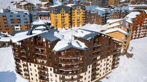 Et hotel med flere etager, altaner, sneklædte tage og en ski slope i baggrunden.