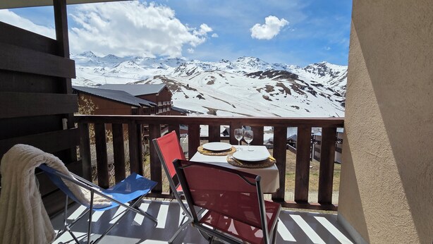 En balkon med et bord dækket til to, med udsigt over snedækkede bjerge.