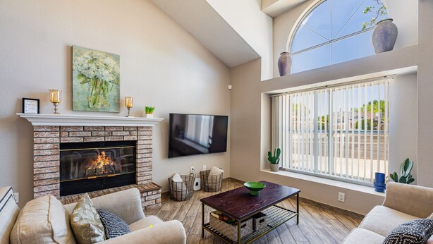 A living room with a fireplace, a flat-screen TV, and a large window with a view. - Taylor Ranch Respite - Modern, Light, Open Concept (Albuquerque)