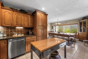 Una cocina con armarios de madera, lavavajillas, una mesa de madera y una zona de comedor con sillas.