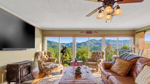 A living room with a fireplace, leather sofa, and a large window with a mountain view.