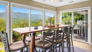 A dining area with a table and chairs, large windows with a mountain view, and a ceiling fan.