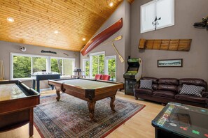 A pool table, a sofa, a canoe, and a view of the outdoors.