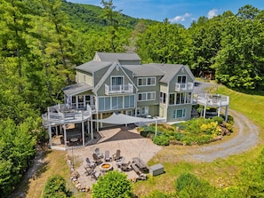 A large, multi-story house with a deck, outdoor seating, and a fire pit.