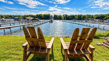Zwei Holz-Adirondack-Stühle blicken auf eine Marina mit vertäuten Booten, eine Anlegestelle erstreckt sich ins Wasser, und der Himmel ist wolkenlos.