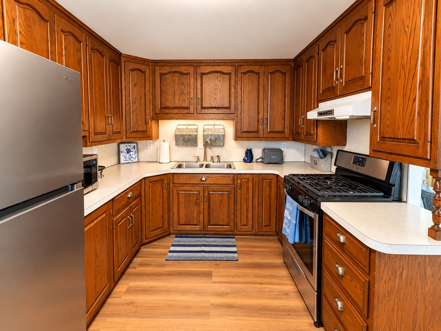 A kitchen with wooden cabinets, a stainless steel refrigerator, a built-in oven, and a microwave.