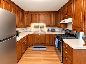 A kitchen with wooden cabinets, a stainless steel refrigerator, a built-in oven, and a microwave. - Cozy cottage with Lake Freeman access, within walking distance to Madam Carroll (Monticello)