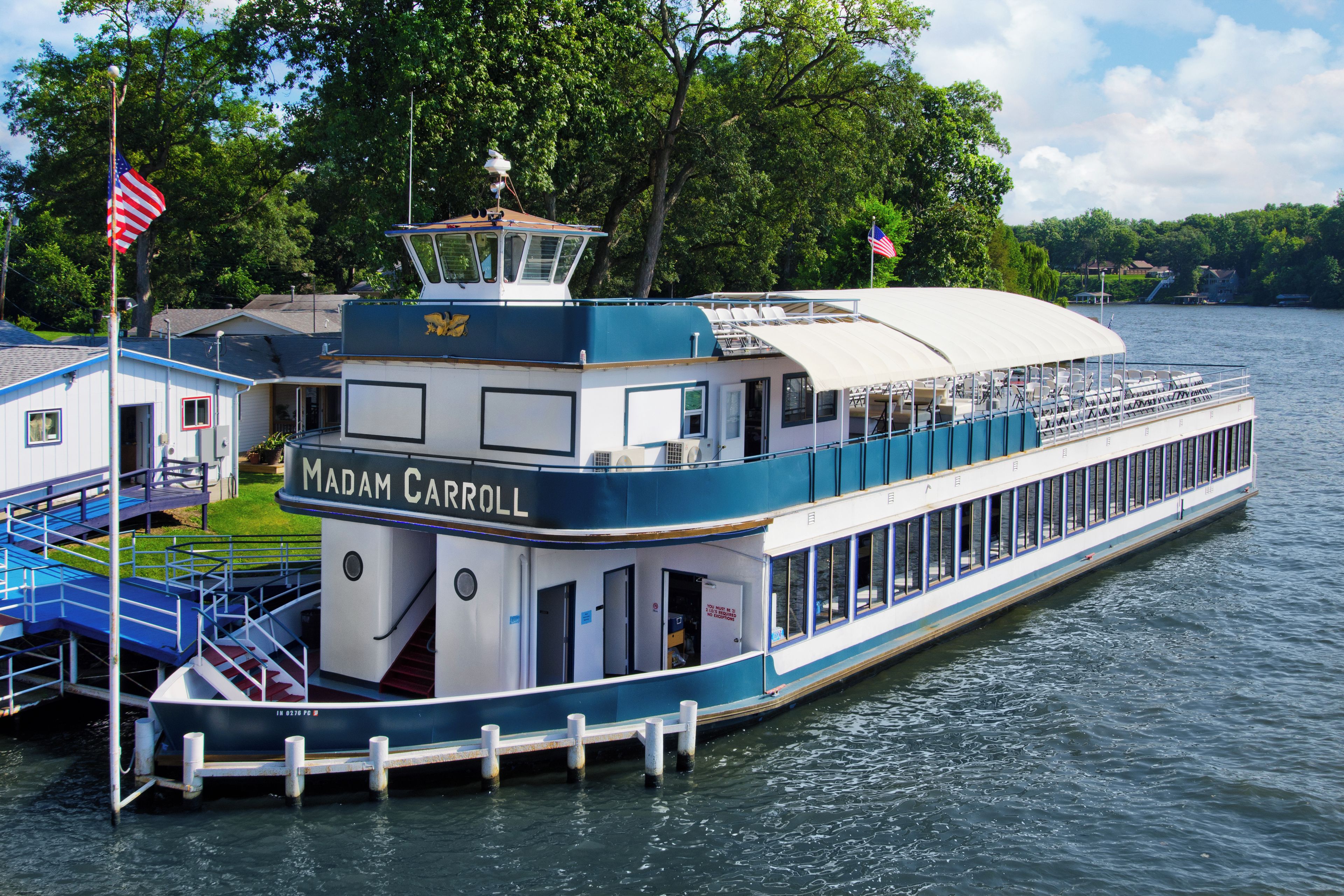 A riverboat named 'Madam Carroll' docked at a pier with a covered deck and a small building adjacent to it.