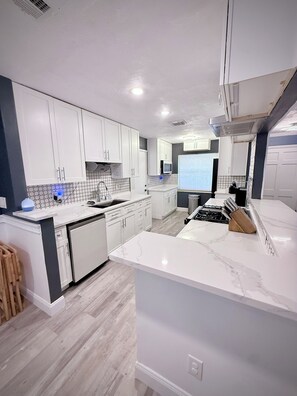 Una cocina moderna con armarios blancos, encimera de mármol y placa de cocina integrada.