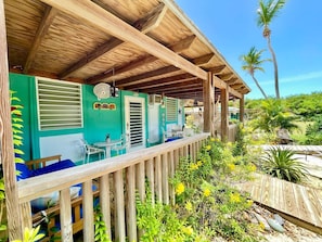 Une terrasse en bois avec un espace salon couvert, une petite table et un ventilateur.