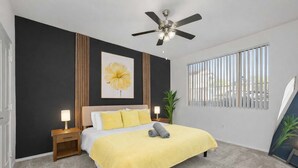 A bedroom with a bed, bedside tables, a ceiling fan, a window with blinds, and a large flower painting on the wall. - Scottsdale Oasis Retreat  Pool, BBQ, EV Parking (Scottsdale)