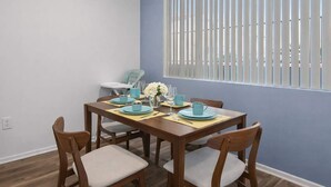 A dining area with a wooden table set for four, a high window with blinds, and a blue wall. - Scottsdale Oasis Retreat  Pool, BBQ, EV Parking (Scottsdale)