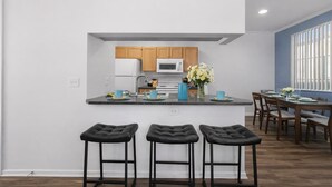 A modern kitchen with wooden cabinets, a central island with bar stools, and a dining area with a blue wall and large windows. - Scottsdale Oasis Retreat  Pool, BBQ, EV Parking (Scottsdale)