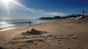 Une plage avec des empreintes de pas et un château de sable, sous un ciel dégagé.