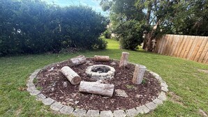 Boccia di fuoco circolare con tronchi e pietre, delimitata da un bordo in pietra, in un giardino sul retro.